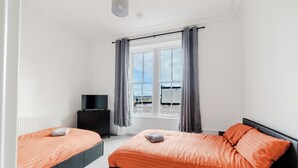 Ein Schlafzimmer mit zwei Betten, einem Fernseher und einem Fenster mit Vorhängen.