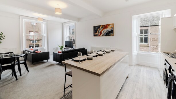 Eine moderne Küche mit Kochinsel, Essbereich mit Stühlen und Tisch sowie Wohnbereich mit Sofa und Fernseher.