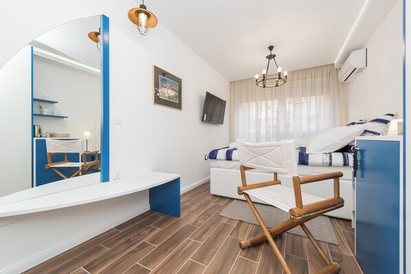 A modern hotel room with a large mirror, a bed with a white and blue striped blanket, a wooden chair, a flat-screen TV, and a large window with curtains. - Blue Old Navy Rooms (Zadar)