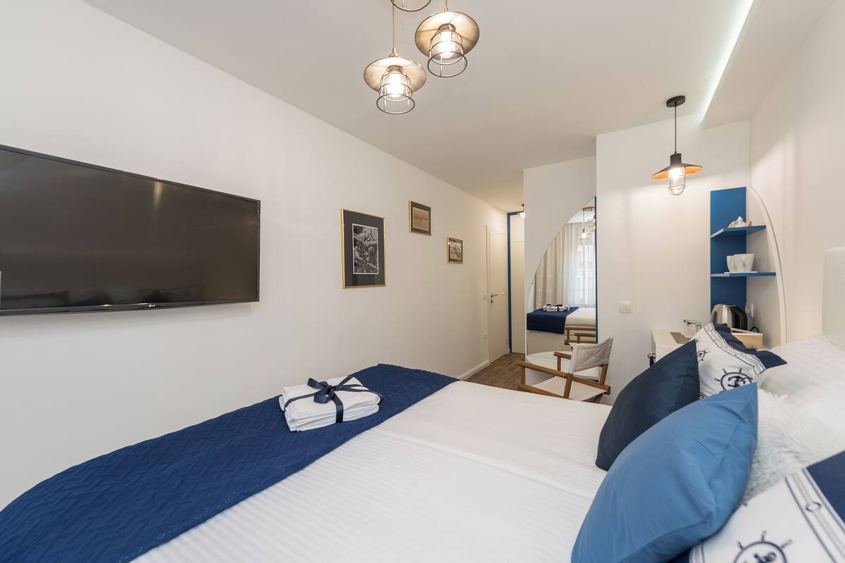 A hotel room with a bed, a flat-screen TV, a desk with a chair, and a mirror.