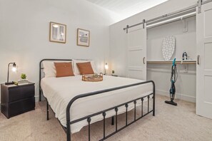 A neatly arranged bedroom with a bed, bedside tables, a wardrobe, and a vacuum cleaner. - Classy Modern Studio with Pool plus Golf Sim (Austin)
