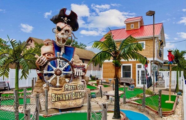 A pirate-themed statue with a steering wheel, surrounded by a pool area and a building with a red roof.