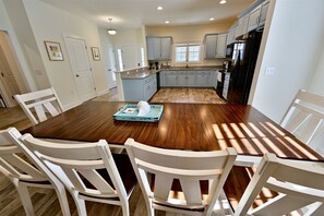 A spacious kitchen with a central island, white cabinetry, and a dining area with a wooden table and white chairs. - New Bethany Beach DE Luxury House in Bethany West: (Bethany Beach)