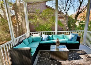 A covered outdoor seating area with a sectional sofa, a coffee table, and a patterned rug.