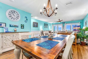 A dining area with a wooden table, blue placemats, and a large wall clock.
