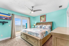 A bedroom with a bed, a ceiling fan, a TV, and a window with curtains.
