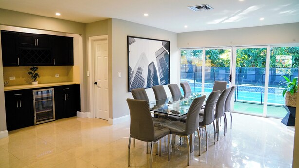 A modern kitchen with dark cabinets, a glass refrigerator, and a dining area with a glass table and chairs.