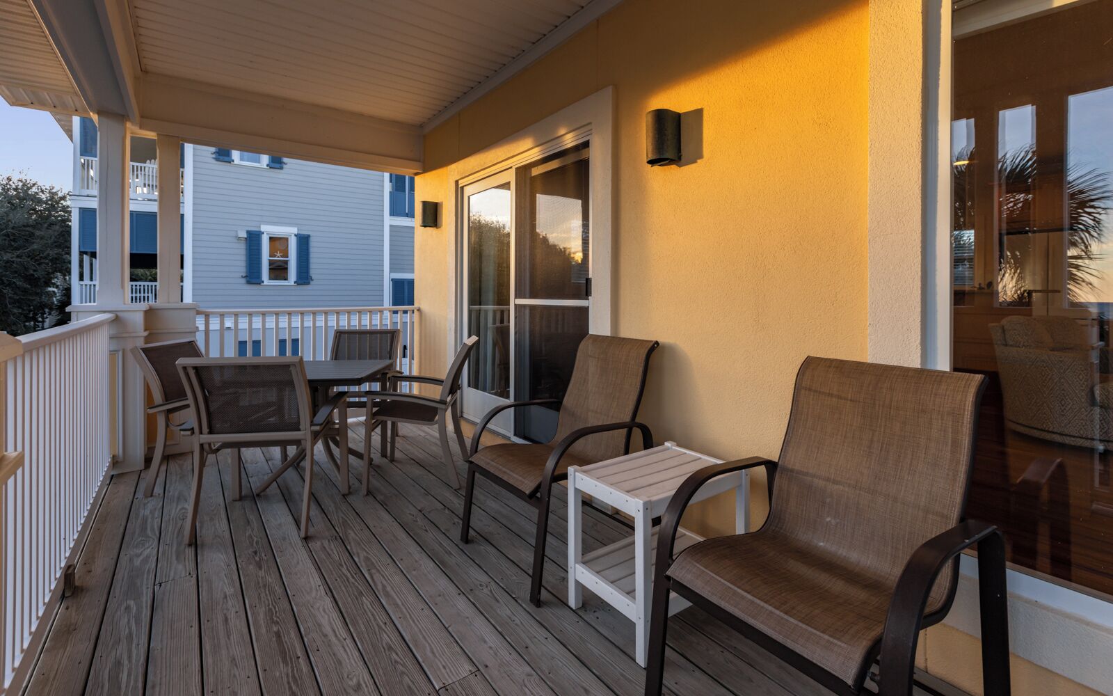 A covered outdoor area with wooden flooring, a white railing, and seating including chairs and a table.