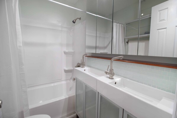 A modern bathroom with a glass shower enclosure, a white bathtub, and a vanity with a mirror.