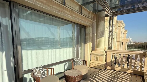 A sunlit balcony with a glass enclosure, two cushioned chairs, a small round table, and a patterned cushion. - Reikartz Qarshi (Qarshi)