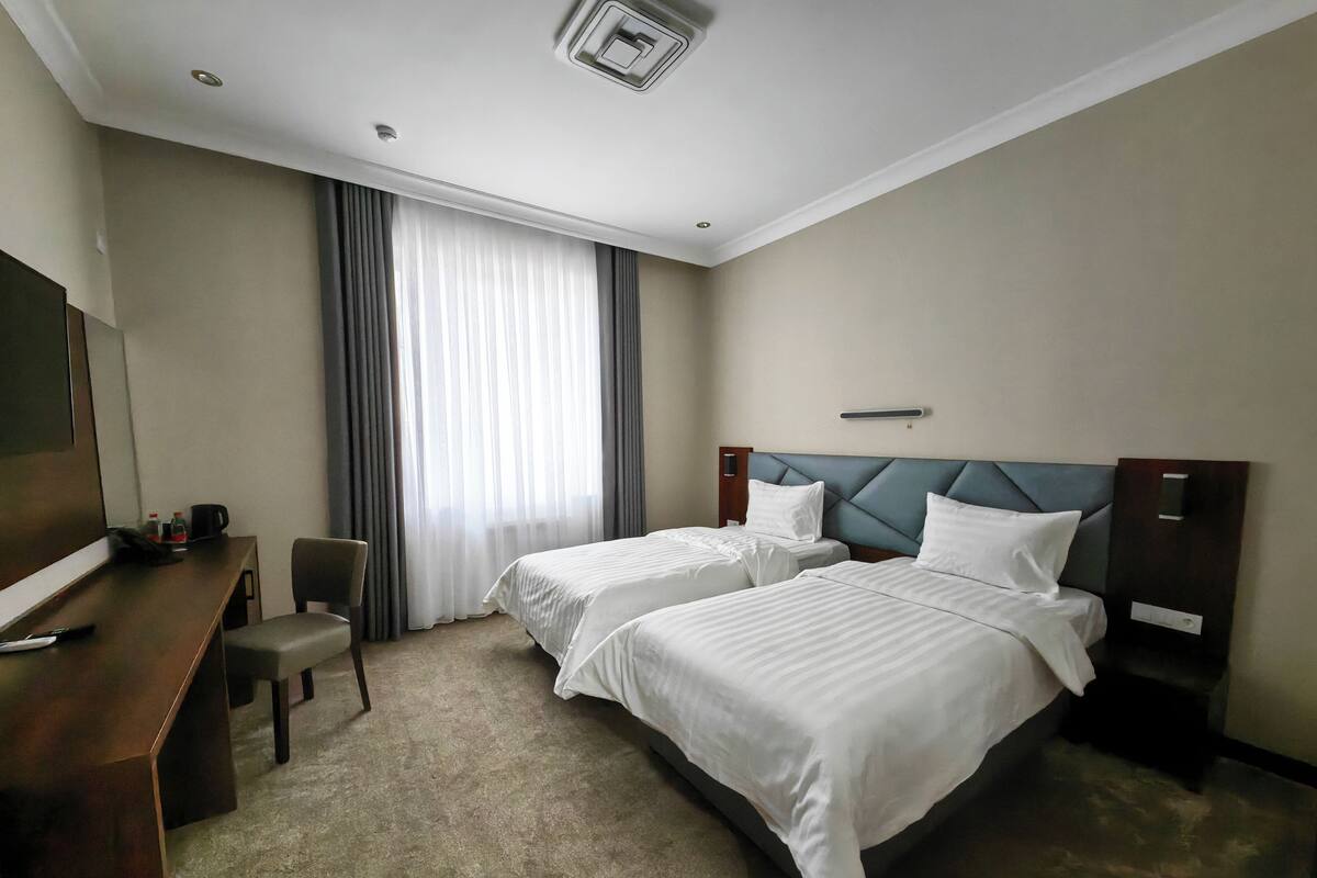 A hotel room with two beds, a desk, a chair, and a large window with curtains.