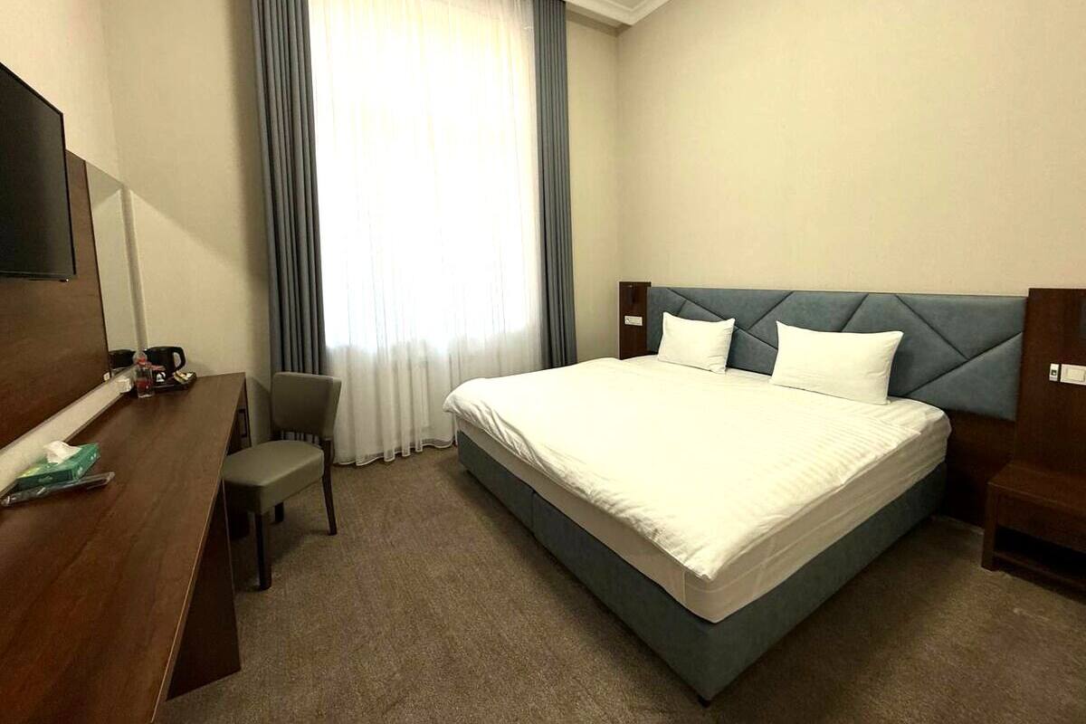 A hotel room with a large bed, a desk, a chair, and a TV.