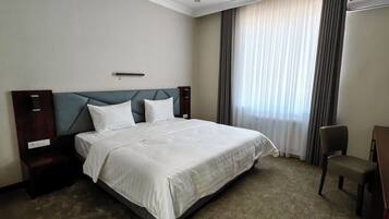 A hotel room with a large bed, a nightstand, a desk, and a chair.