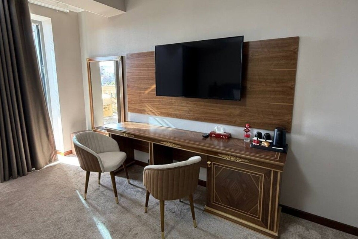 A hotel room with a wooden desk, two chairs, a flat-screen TV mounted on the wall, and a coffee machine on the desk.