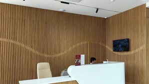 A reception desk with a wooden backdrop and a mounted TV. - Reikartz Qarshi (Qarshi)