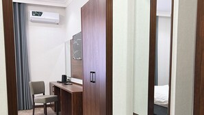 A hotel room with a desk, chair, and a large mirror. There is a wardrobe, a bed, and an air conditioning unit on the wall. - Reikartz Qarshi (Qarshi)