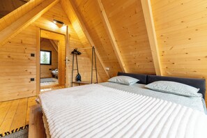 A cozy wooden cabin bedroom with a lofted sleeping area, a bed with white bedding, and a window with a view of a tree. - Mountain homes Durmitor 2 (Uskoci)
