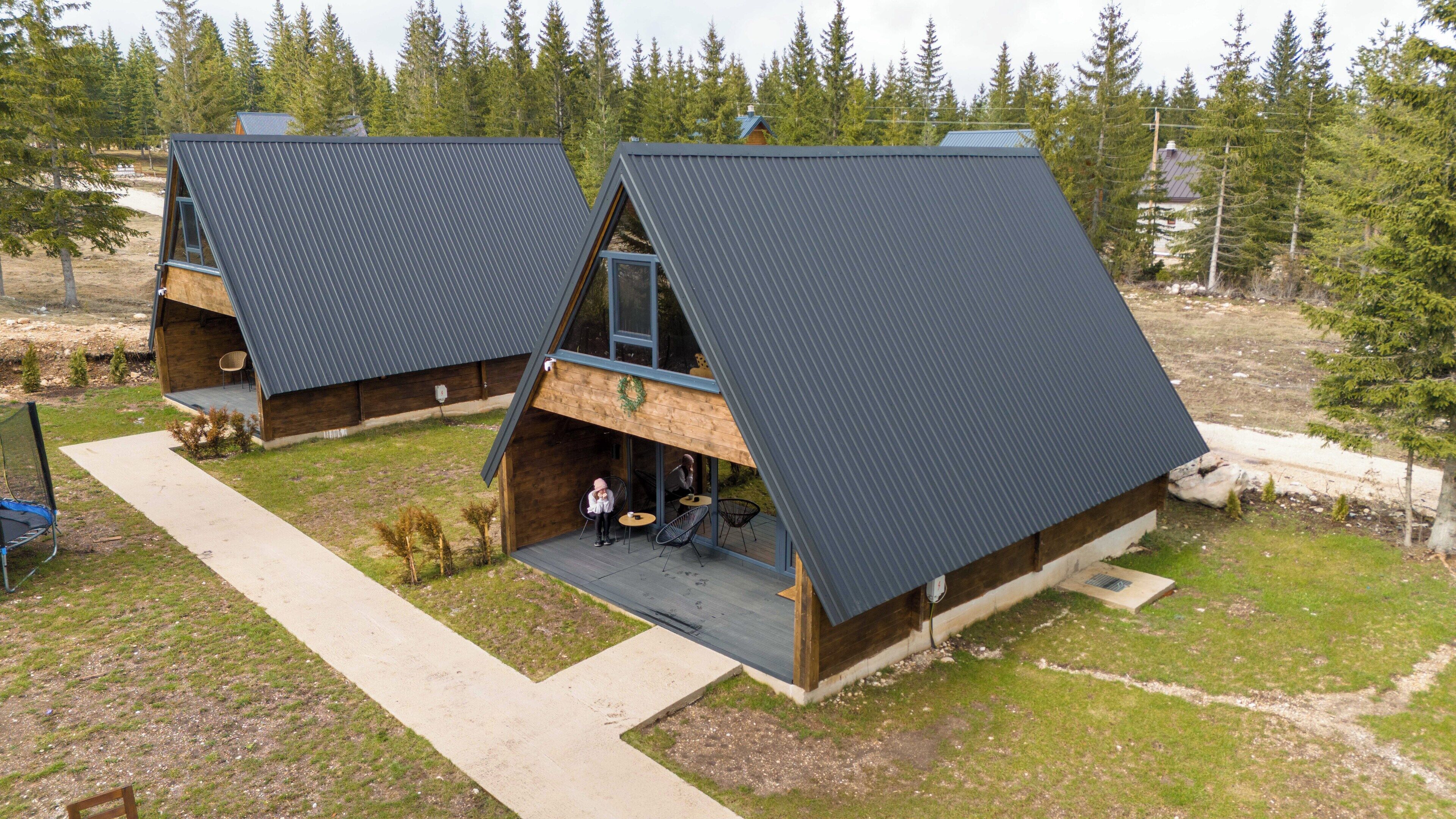 A modern cabin with a sloped roof, a wooden deck, and a small outdoor seating area.