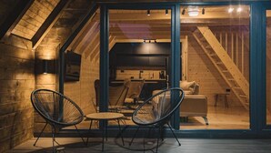 A cozy attic room with a wooden interior, a glass door leading to a dining area with two chairs and a table, and a staircase in the background. - Mountain homes Durmitor 2 (Uskoci)