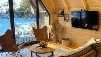 Un interior de madera acogedor con un sofá, una mesa de comedor con fruta y un televisor en la pared.
