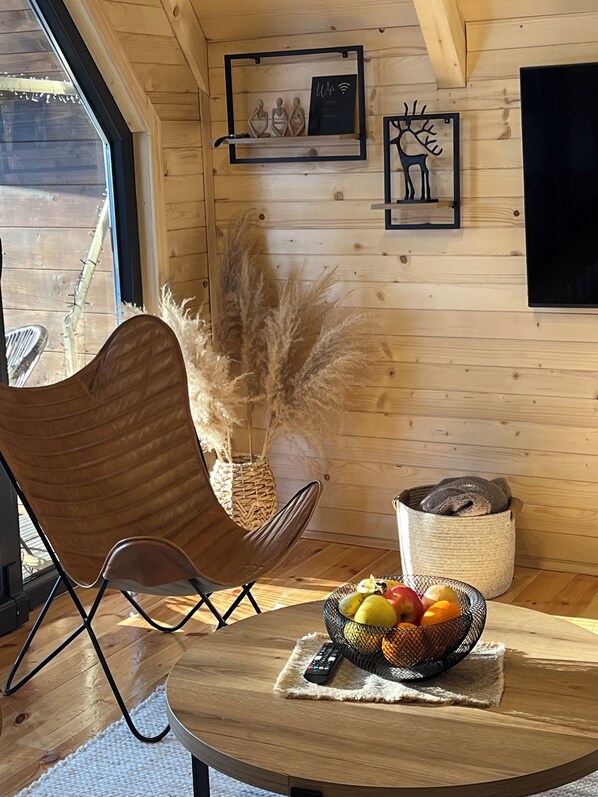 A wooden interior with a round table, a cushioned chair, a woven basket with fruits, and wall-mounted decor. - Mountain homes Durmitor 2 (Uskoci)
