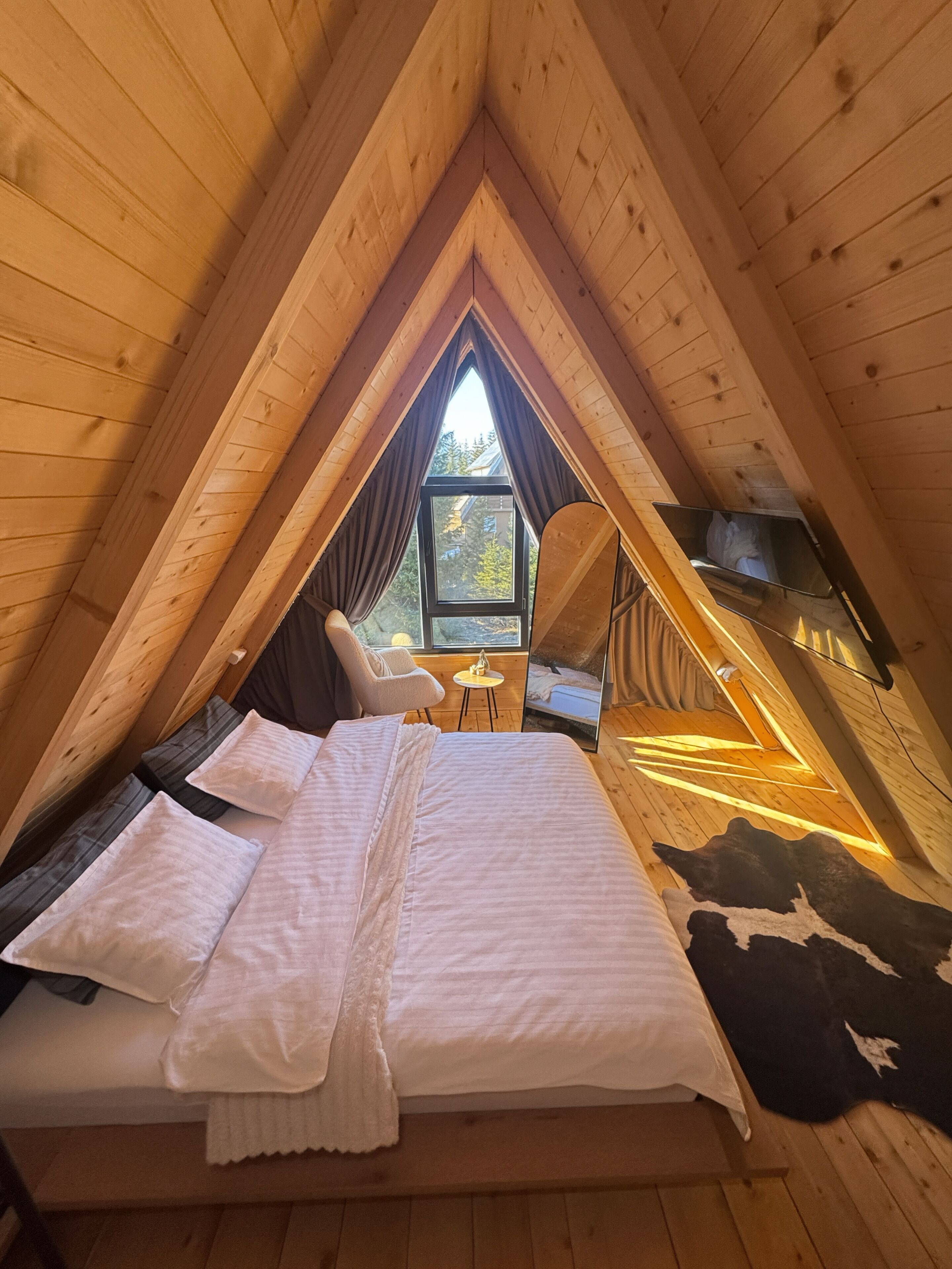 A cozy attic bedroom with a bed, a chair, a small table, and a window.