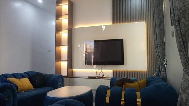 Een moderne woonkamer met een flatscreen televisie aan een wand, een blauwe zithoek en een ronde salontafel.