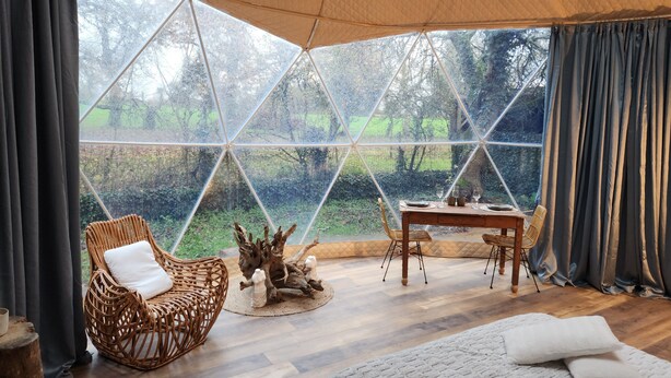 Una habitación acogedora con un ventanal grande, una mesa de madera, una silla de mimbre y una cama.