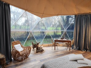 Una habitación acogedora con un ventanal grande, una mesa de madera, una silla de mimbre y una cama.
