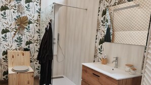 Baño con inodoro de madera, ducha con puerta de vidrio, lavamanos blanco con espejo y tocador de madera.