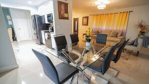 Ein modernes Wohnzimmer mit einem Glastisch, schwarzen Stühlen, einer Couch und einem Fernseher.