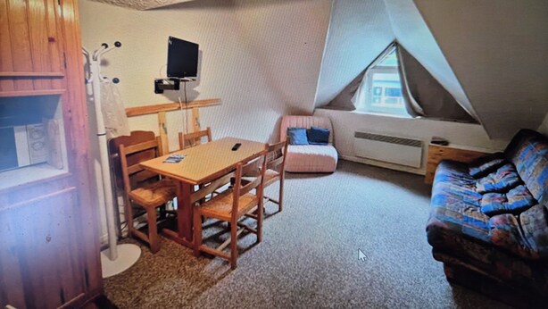 A compact room with a sloped ceiling, a wooden dining table with chairs, a small sofa, and a television mounted on the wall. - Studio le lioran "les sagnes (Laveissière)