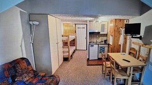 A compact room with a sofa, a small dining table, a kitchen area, and a television mounted on the wall. - Studio le lioran "les sagnes (Laveissière)