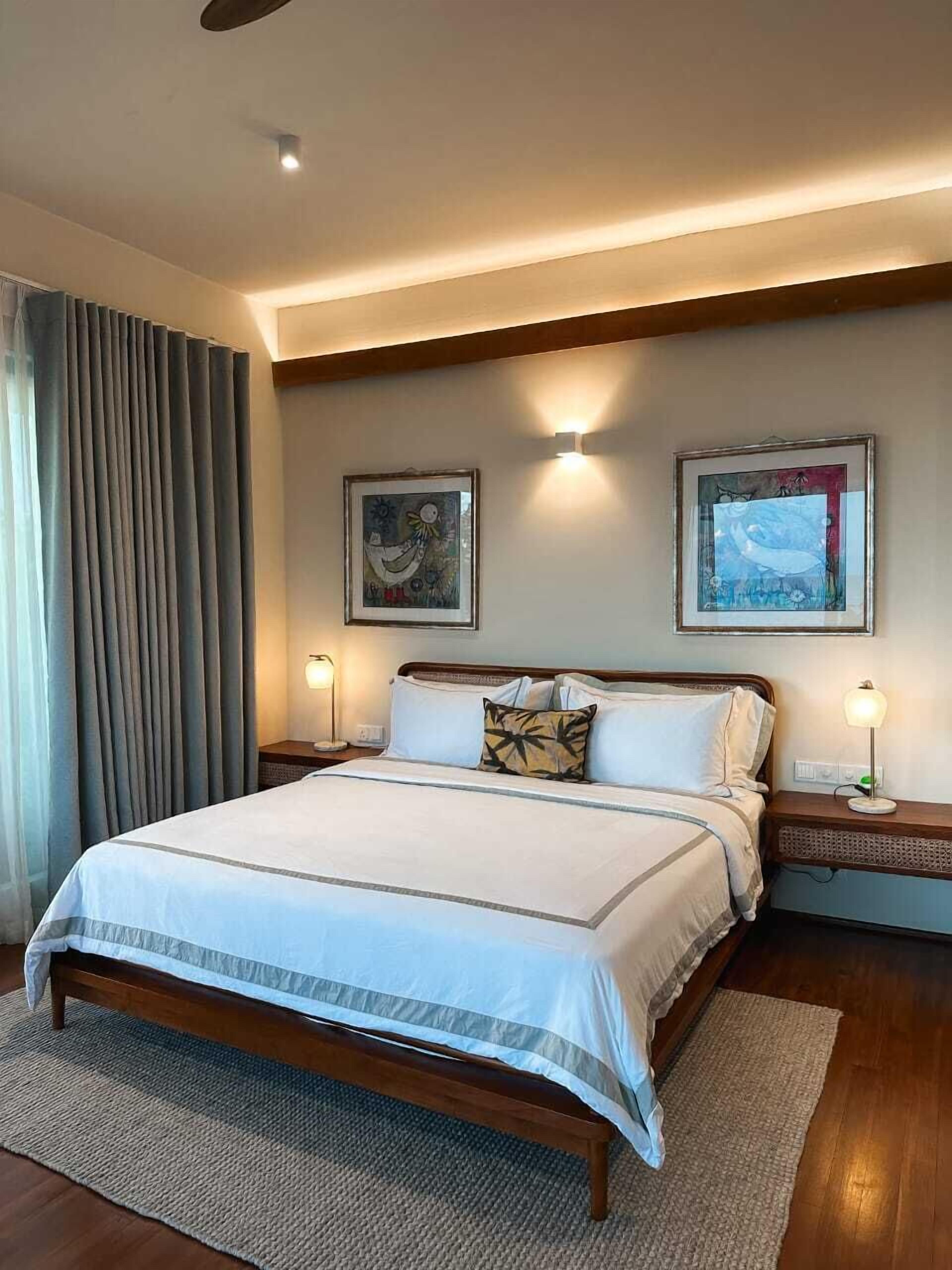 A neatly arranged bedroom with a large bed, two bedside tables with lamps, and two framed artworks on the wall.