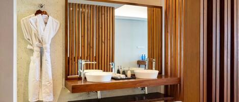 A modern bathroom with a large mirror, two sinks, a robe rack, and a bathtub.