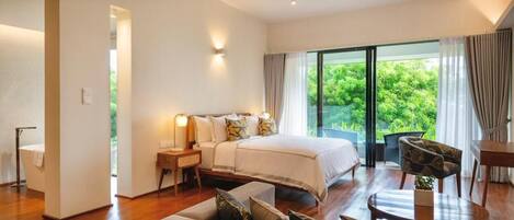 Une chambre spacieuse avec un grand lit, un coin salon avec un canapé et une table, et un balcon offrant une vue sur la verdure.