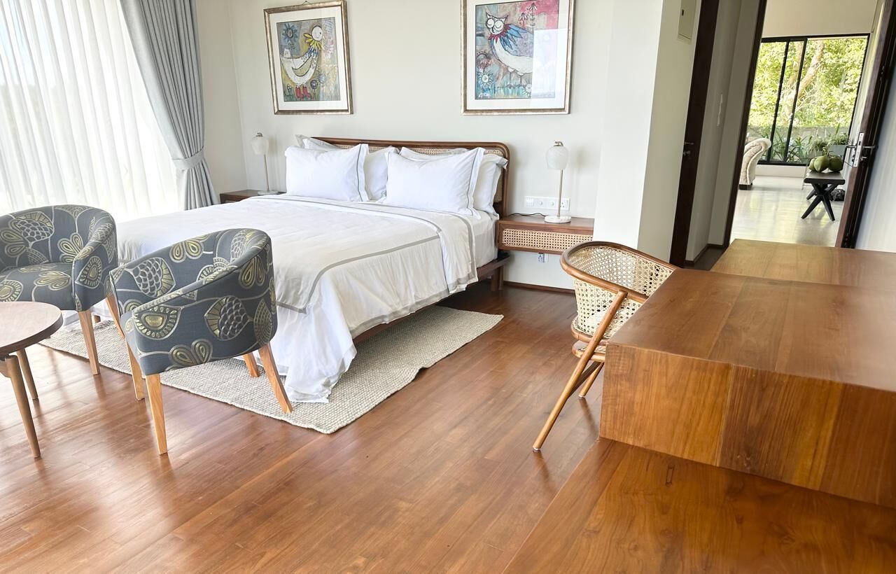 A bedroom with a bed, two chairs, a wooden table, and artwork on the wall.