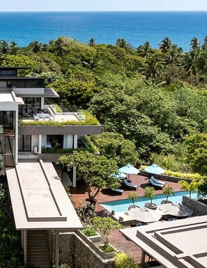 Un resort moderno con piscina en la azotea, exuberante vegetación y vista al océano.