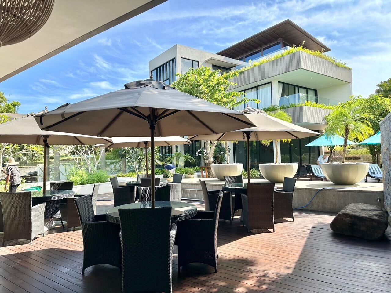 An outdoor patio with tables and chairs, umbrellas, and a modern building in the background.