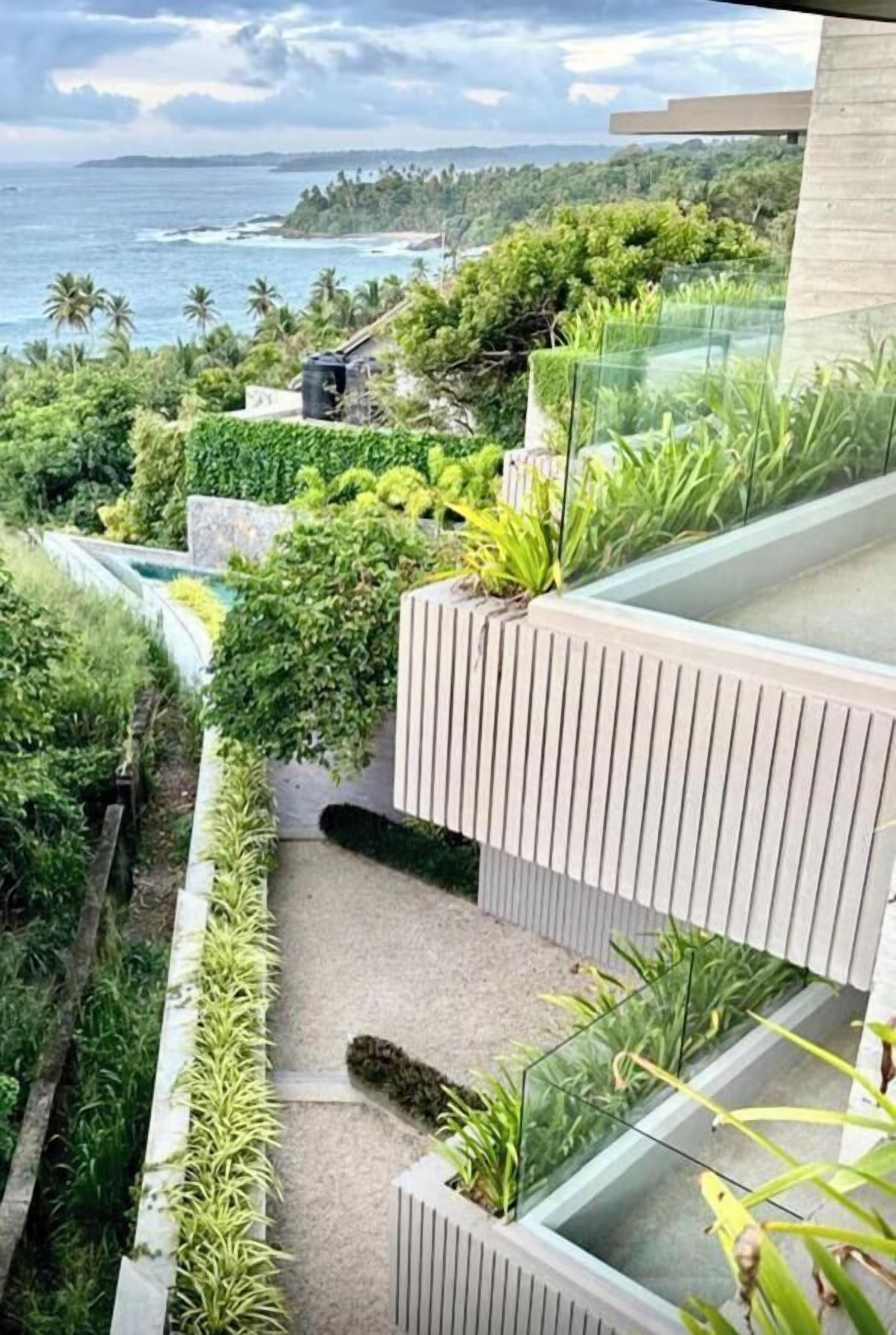A modern outdoor balcony with lush greenery and a view of the ocean.
