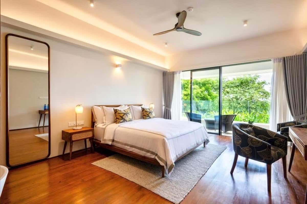 A modern bedroom with a large bed, bedside tables, a mirror, and a view of greenery outside.