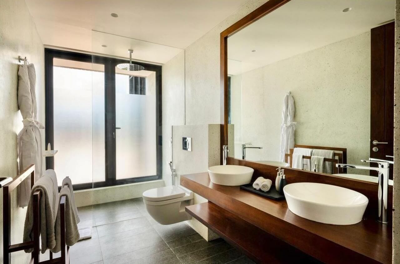 A modern bathroom with a large mirror, two sinks, a toilet, and a shower area.