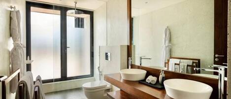 A modern bathroom with a large mirror, two sinks, a toilet, and a shower area.