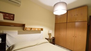 Un dormitorio con cama, un armario de madera, una mesita de noche con lámpara y una estantería en la pared.