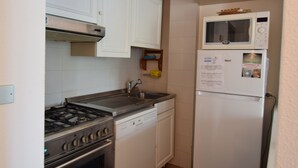 Cocina compacta con armarios blancos, estufa de acero inoxidable, lavavajillas, microondas y refrigerador.