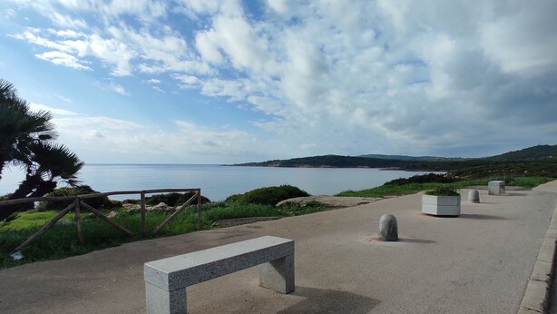 Un camino empedrado con un banco de piedra, una valla de madera y vistas al mar y las colinas.