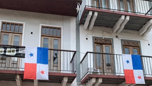 Un edificio con balconi, porte in legno e due bandiere.