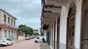 Una strada con auto parcheggiate e un furgone bianco. Si vedono edifici con balconi e finestre lungo il marciapiede.