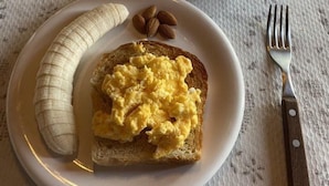 Un piatto con uova strapazzate su pane tostato, una banana e mandorle, insieme a una tazza di caffè.