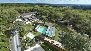 Een woonhuis met een zwembad, een tennisbaan en een groot huis omringd door bomen.